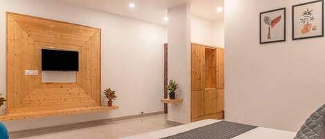 A modern hotel room with a bed, a TV mounted on a wooden wall, a wardrobe, and a small plant.