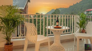 A balcony with two white wicker chairs, a small round table with a bottle and glasses, and potted plants. - The Green Land Kasauli  (Kasauli)