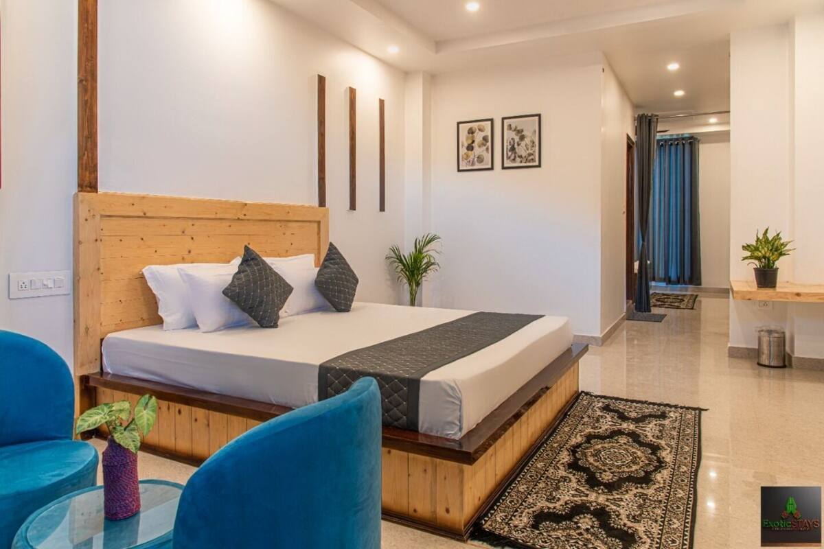 Een moderne hotelkamer met een bed met houten hoofdbord, een klein bureau, een blauwe stoel en een kamerkleed met patroon.