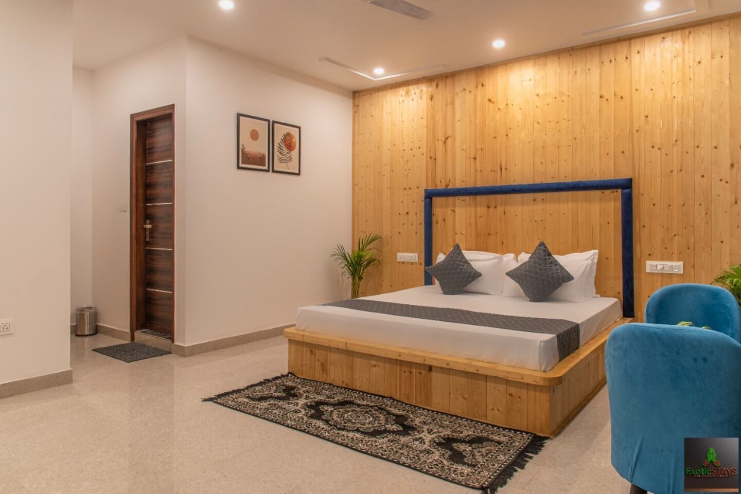 A bedroom with a wooden headboard, a bed with pillows, a blue chair, and a patterned rug.
