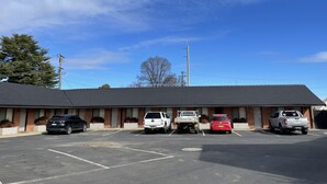 Un motel avec un parking, plusieurs voitures garées et un ciel bleu dégagé.