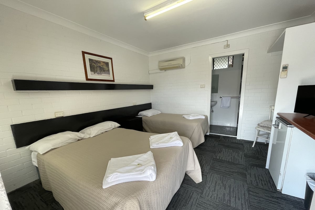 A hotel room with two beds, a desk, a chair, a TV, and a bathroom visible through an open door.