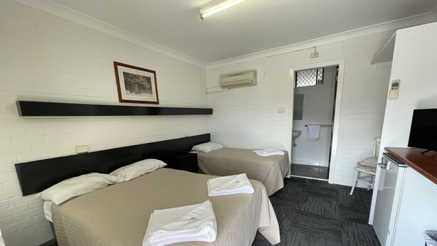 Une chambre d’hôtel avec deux lits, un bureau, une chaise, une télévision et une salle de bain visible à travers une porte ouverte.