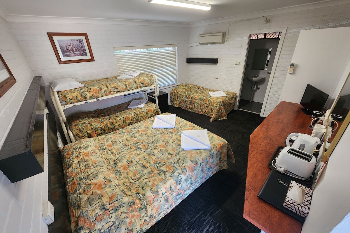 A room with two beds, a desk with a computer, a sink, and a framed picture on the wall.
