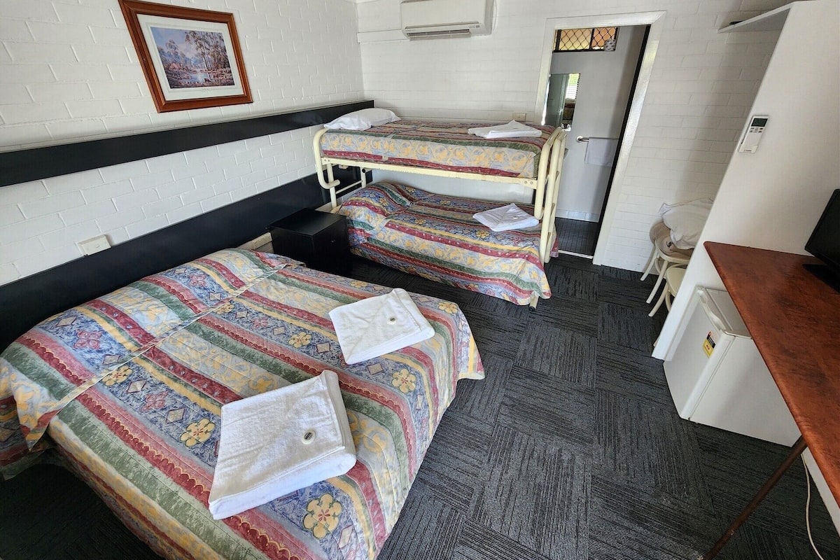 A room with two beds, a desk, a chair, and a picture on the wall.