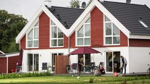 Ett tvåvåningshus med en röd fasad och vita detaljer, med stora fönster och en täckt uteplats.