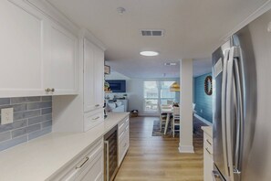 Una cocina moderna con armarios blancos, un refrigerador de acero inoxidable y un comedor con una pared de acento azul.