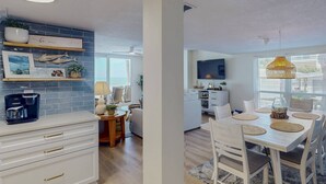 Una cocina moderna con cafetera, un comedor con televisor y un espacio de sala con un amplio ventanal.