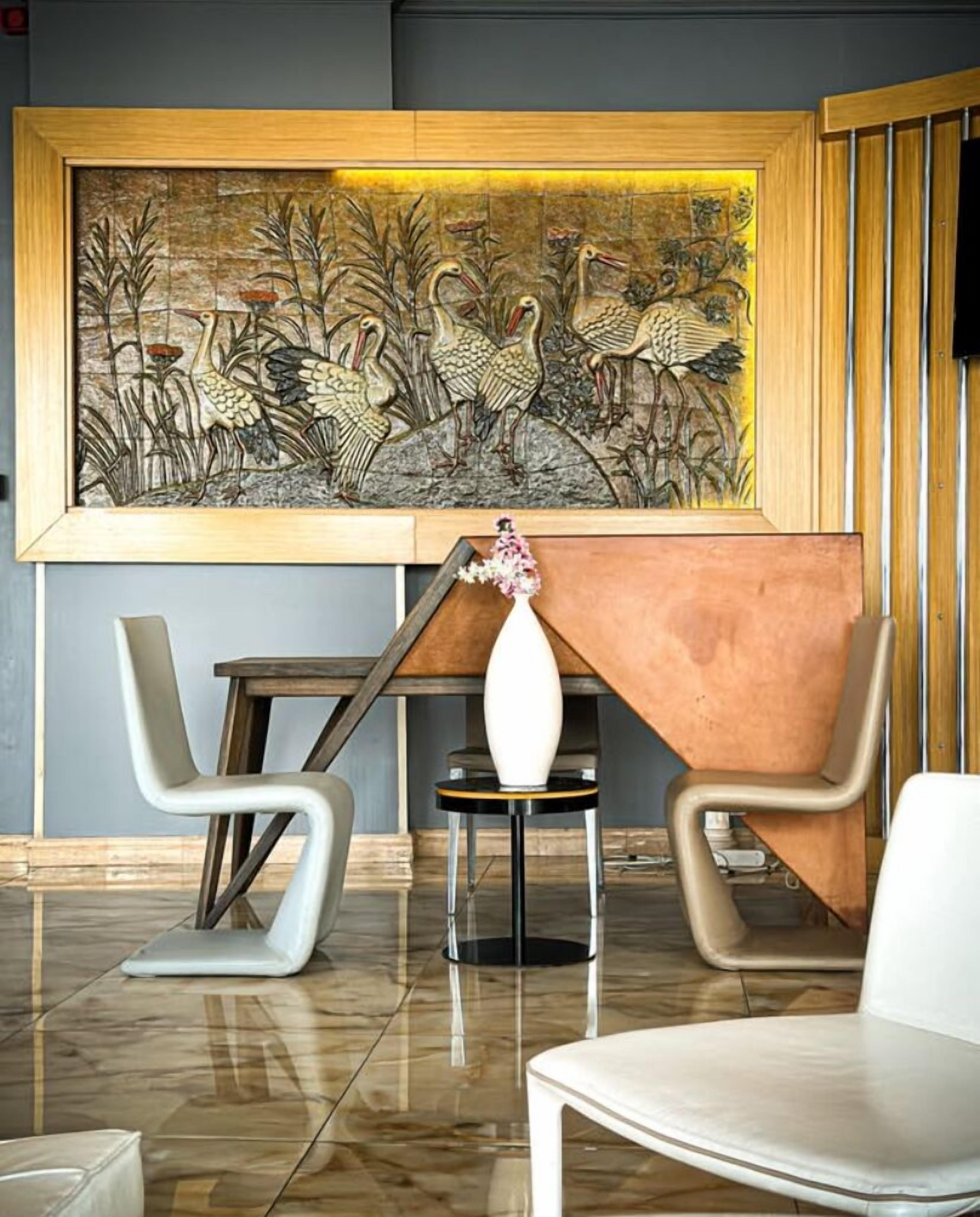 Un hall d’entrée moderne agrémenté d’une grande fresque représentant des oiseaux, de deux fauteuils contemporains, d’une petite table avec un vase et d’un panneau en bois sur le côté droit.