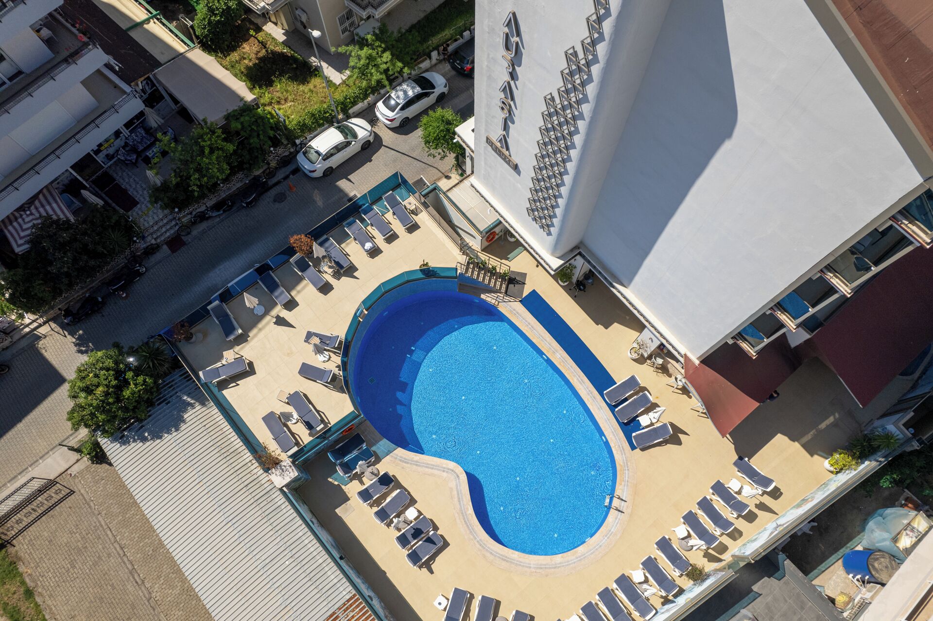 An aerial view of a hotel with a swimming pool surrounded by sun loungers and a small deck area.