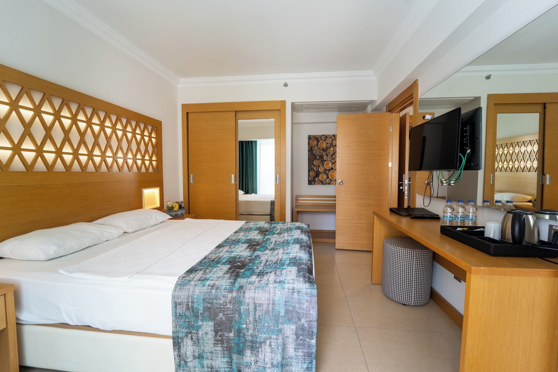Habitación de hotel con cama, escritorio con computadora, televisor y baño visible a través de una puerta abierta.