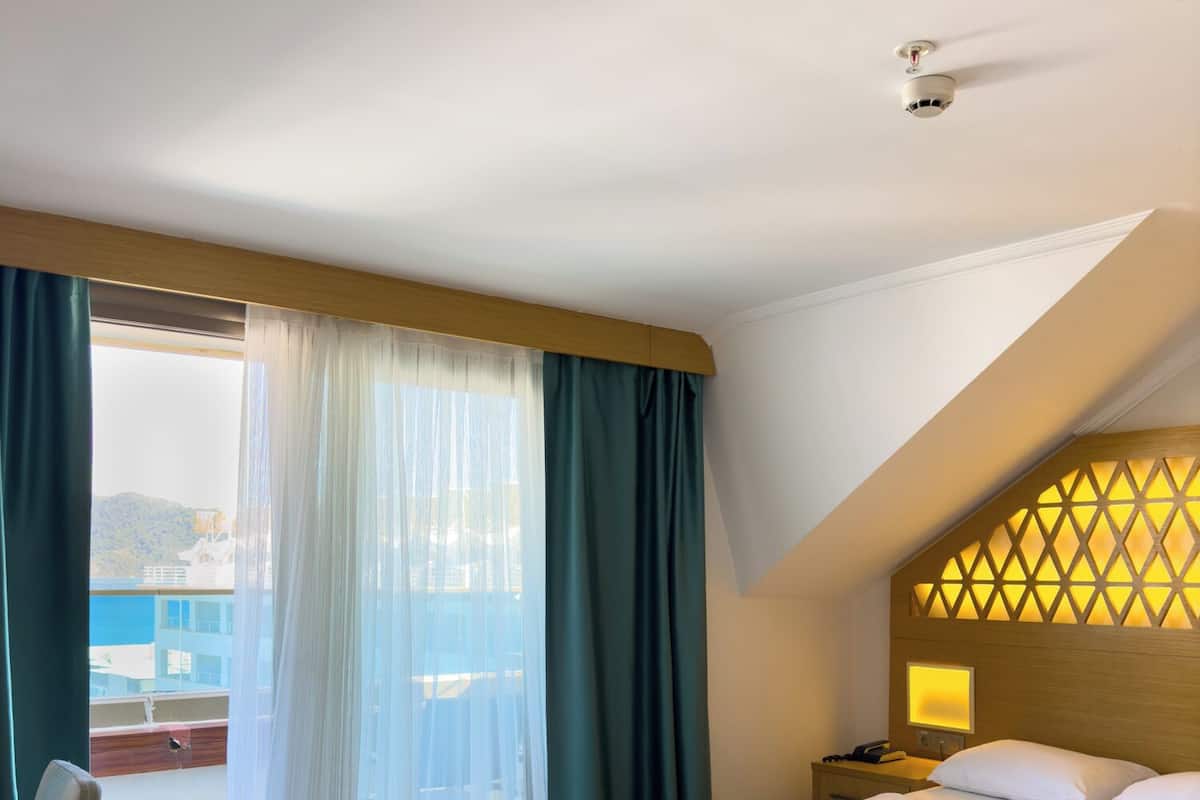 A hotel room with a bed, a desk, a chair, a nightstand, and a view of the outside.