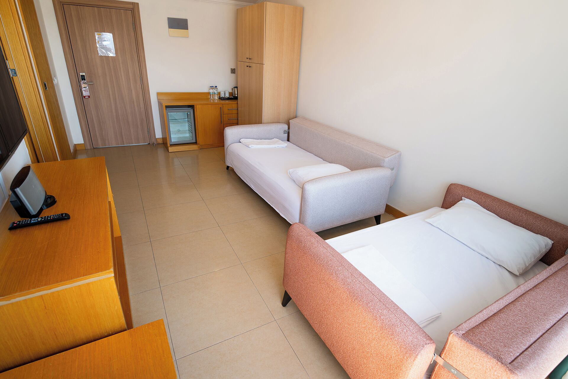 A hotel room with a bed, a sofa, a desk with a computer, a refrigerator, and a door.
