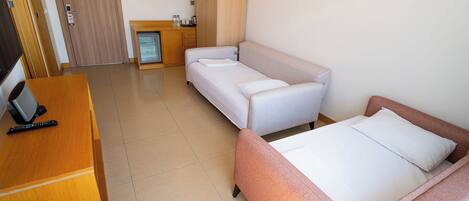 Habitación de hotel con cama, sofá, escritorio con computadora, refrigerador y puerta.