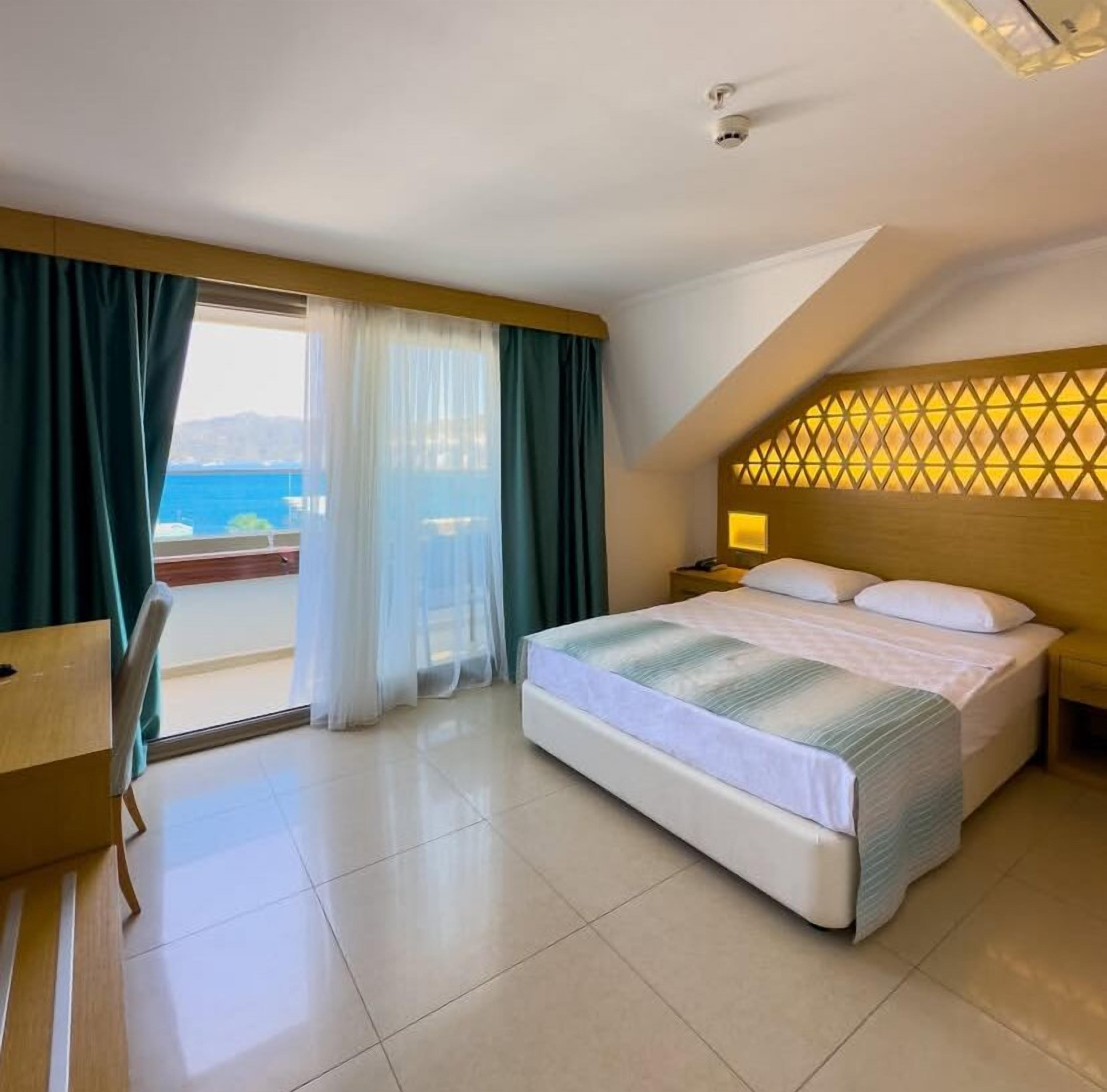 A hotel room with a bed, a desk, and a view of the sea.