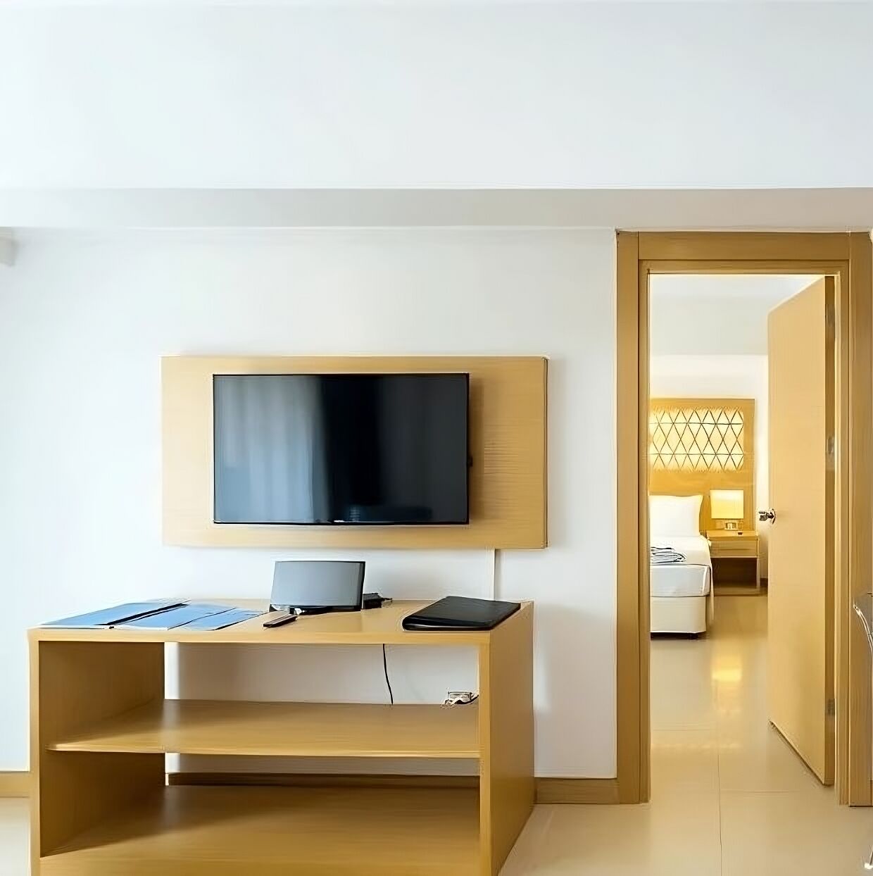 Une chambre d’hôtel avec un téléviseur fixé au mur, un bureau en bois avec un ordinateur portable et un lit avec une tête de lit.