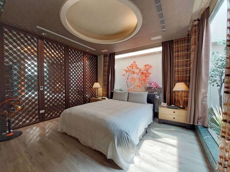 Un dormitorio moderno con una cama grande, separadores de madera y vistas a un árbol.