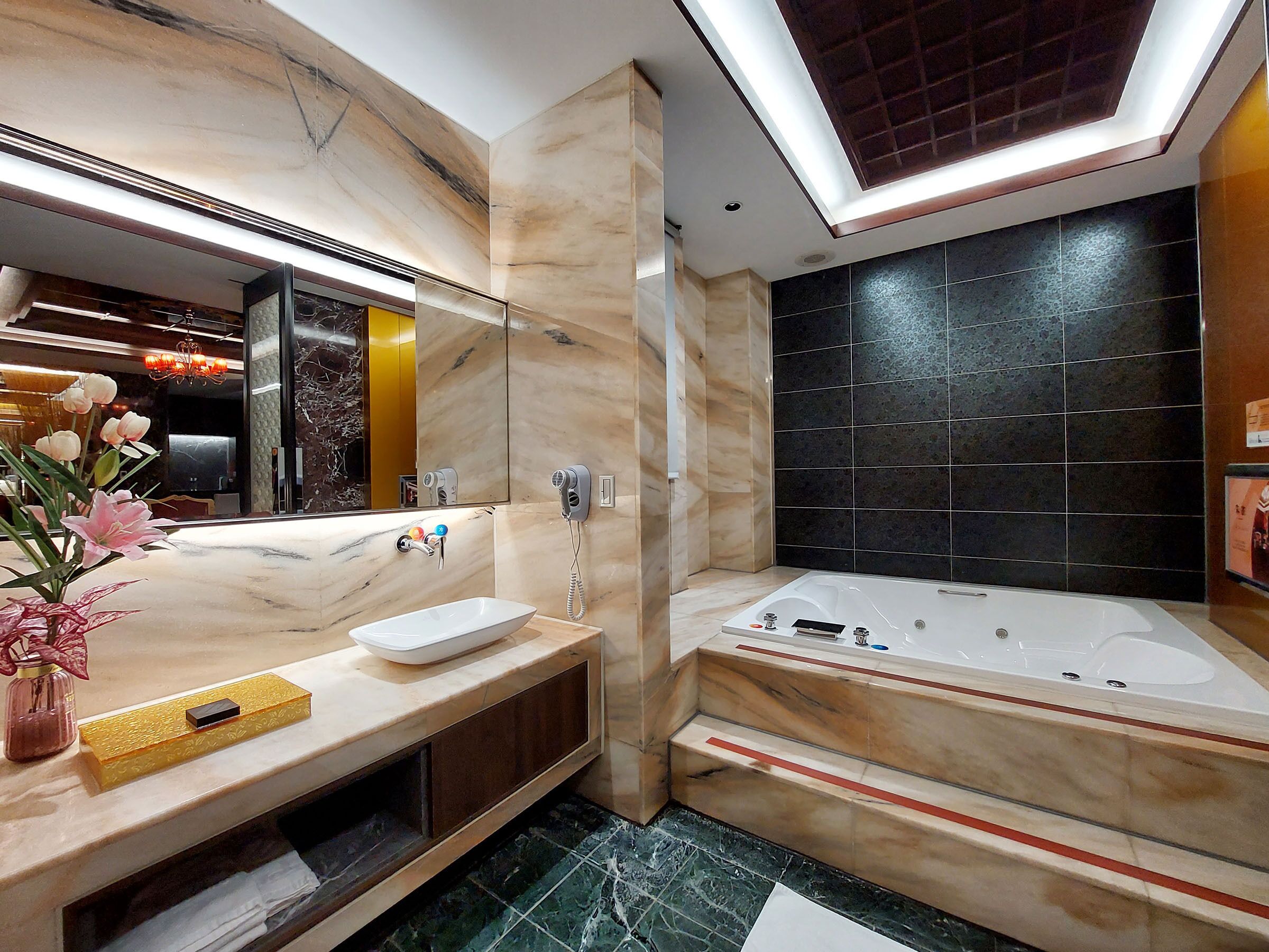 A modern bathroom with a large mirror, a white sink, a vanity, a built-in shower, and a marble floor.