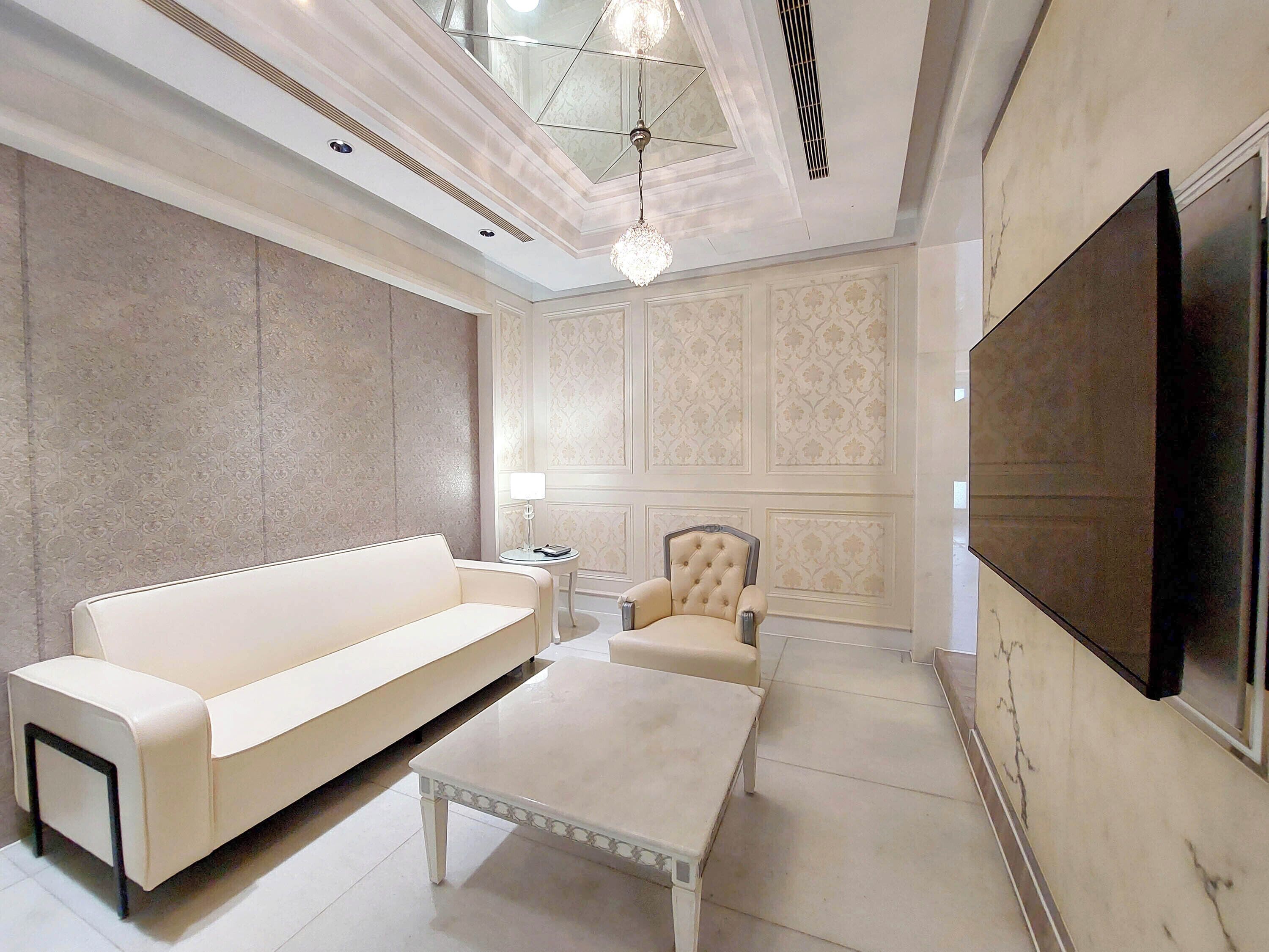 Una sala de estar moderna con un sofá blanco, un sillón capitoné, una mesa de centro y un televisor de pantalla plana montado en la pared.