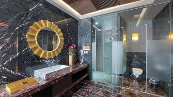 A modern bathroom with a marble vanity, a gold-framed mirror, and a glass-enclosed shower area.