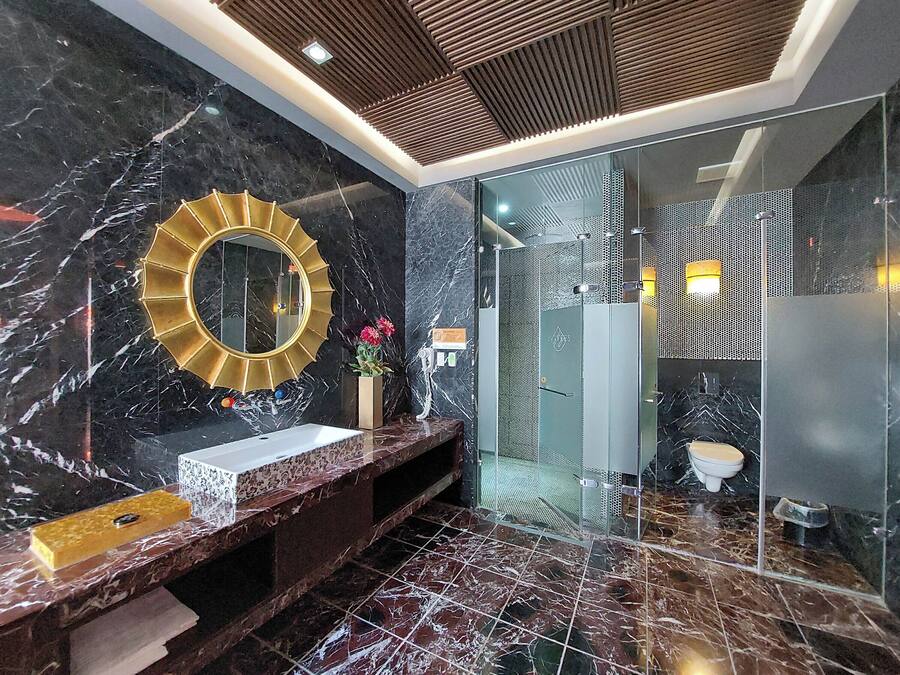 A modern bathroom with a marble vanity, a gold-framed mirror, and a glass-enclosed shower area.