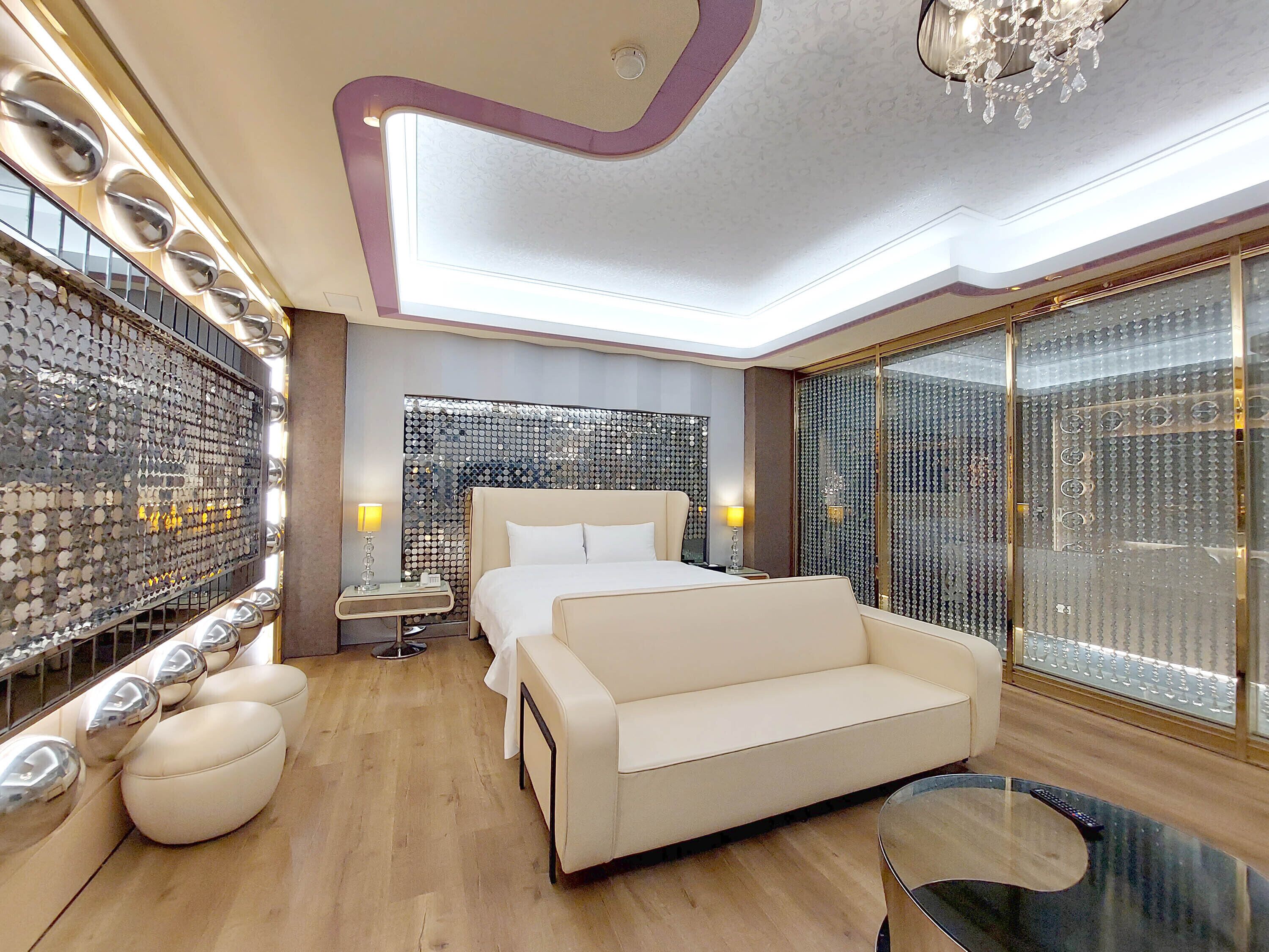 Un dormitorio moderno con una cama grande, un sofá, una mesa de centro de vidrio y una pared decorativa con espejos circulares.