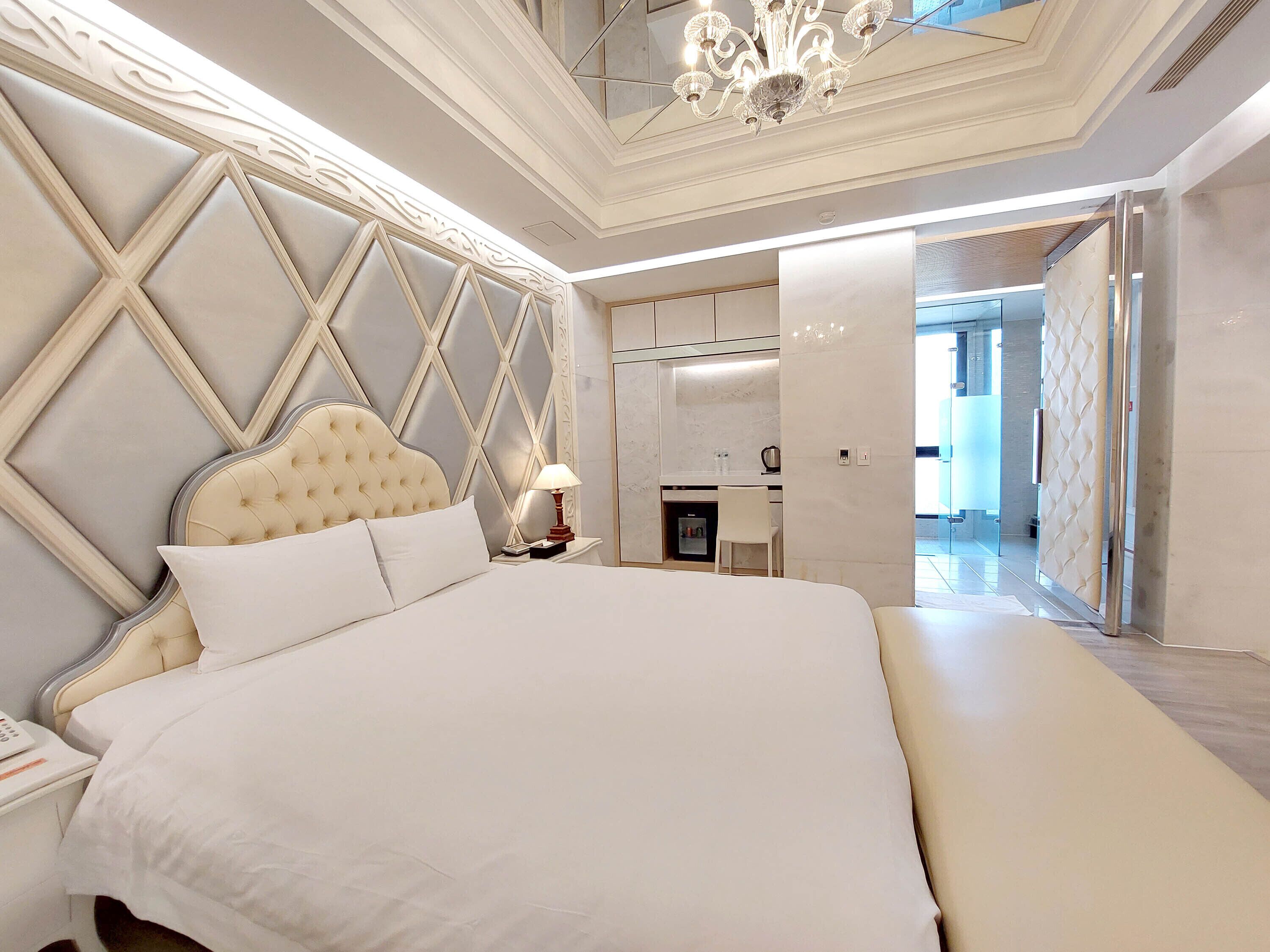 A spacious bedroom with a large bed, a nightstand, a desk, and a chair.