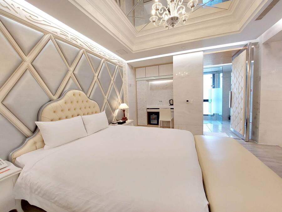 A spacious bedroom with a large bed, a nightstand, a desk, and a chair.