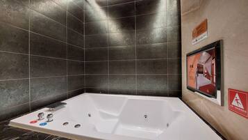 A modern bathroom with a large bathtub, dark patterned tiles, and a framed picture on the wall.