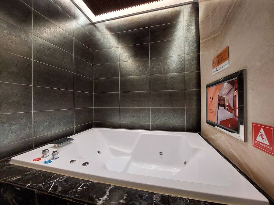 A modern bathroom with a large bathtub, dark patterned tiles, and a framed picture on the wall.