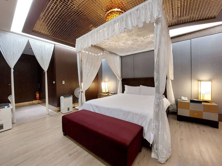 Quarto moderno com cama de dossel, mesa de cabeceira com abajur e um banco vermelho.