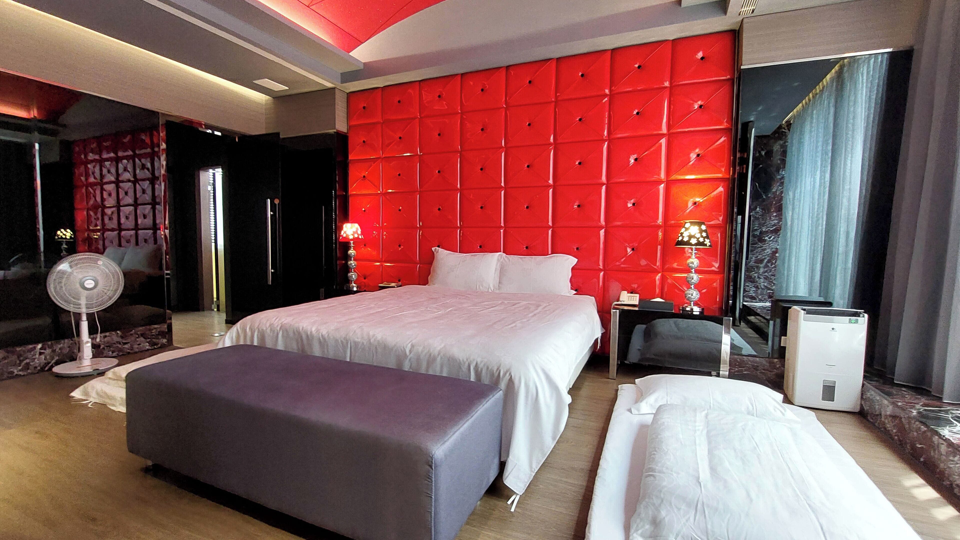 Habitación de hotel con una cama grande, una mesita de noche, una lámpara, un ventilador y una pared de acento roja.