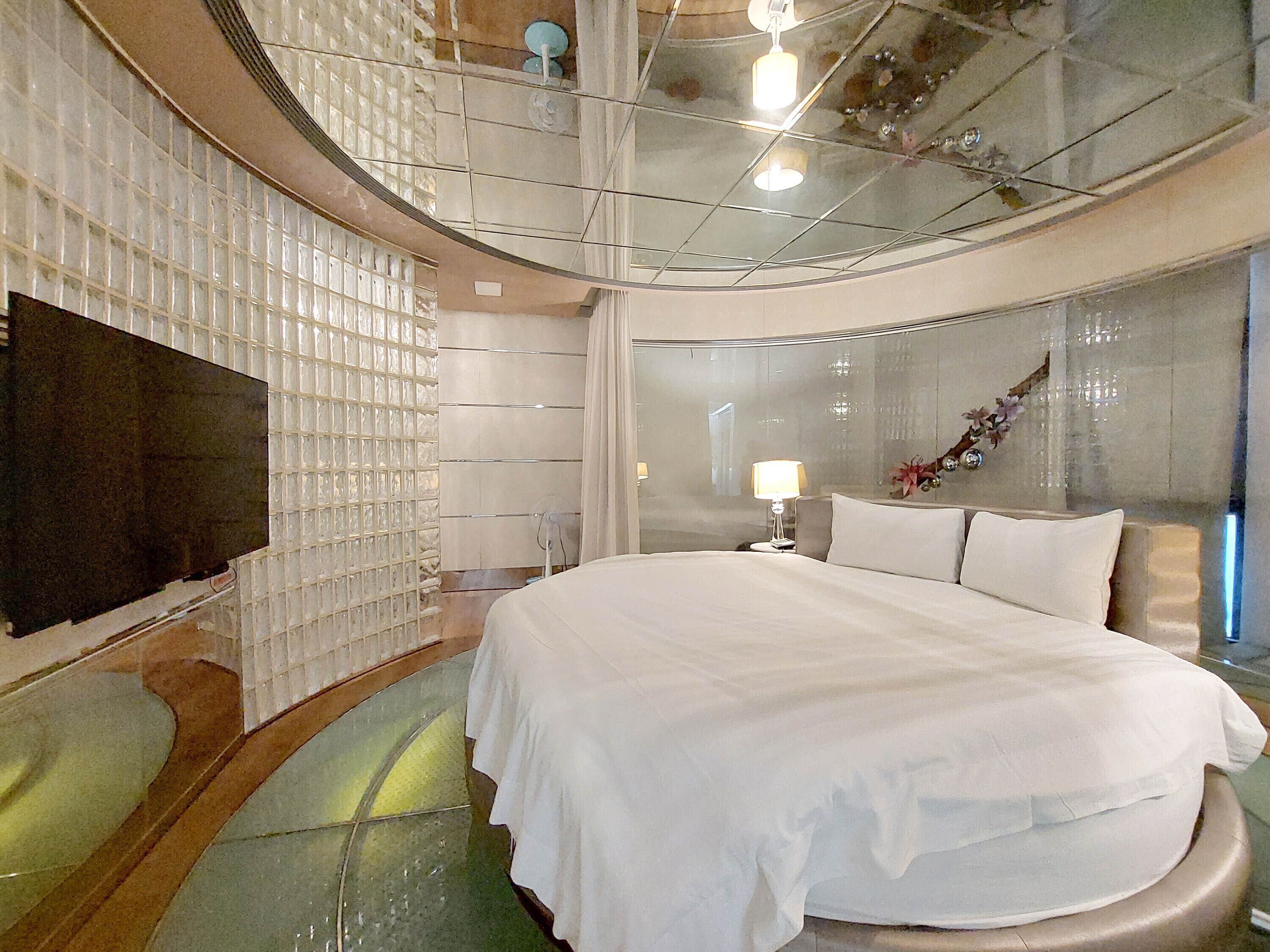 A modern hotel room with a curved ceiling, a large bed, a flat-screen TV, and a glass partition wall.