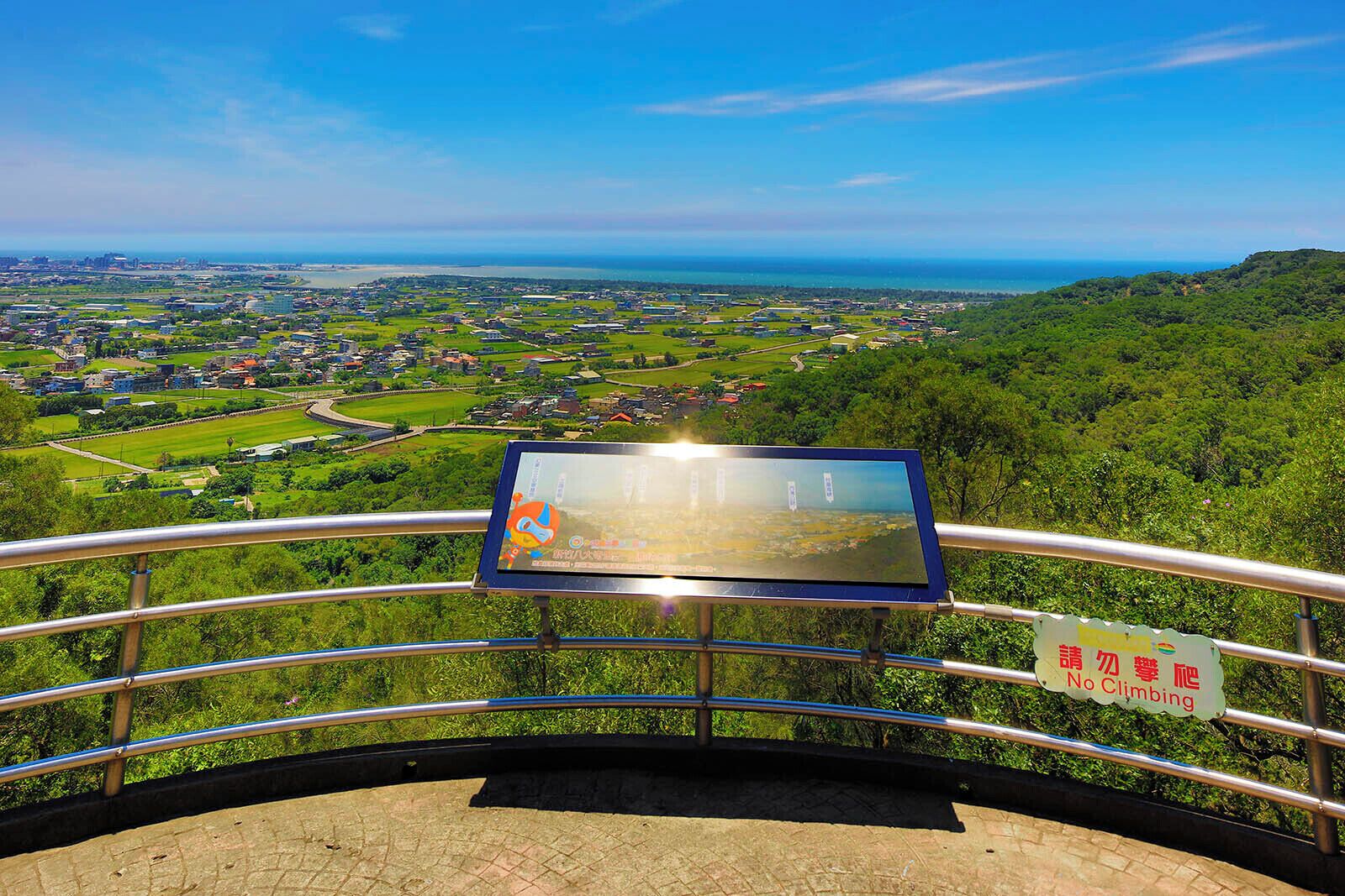 Un mirador panorámico con barandilla metálica, un panel informativo digital y un cartel que dice 'No Climbing'.