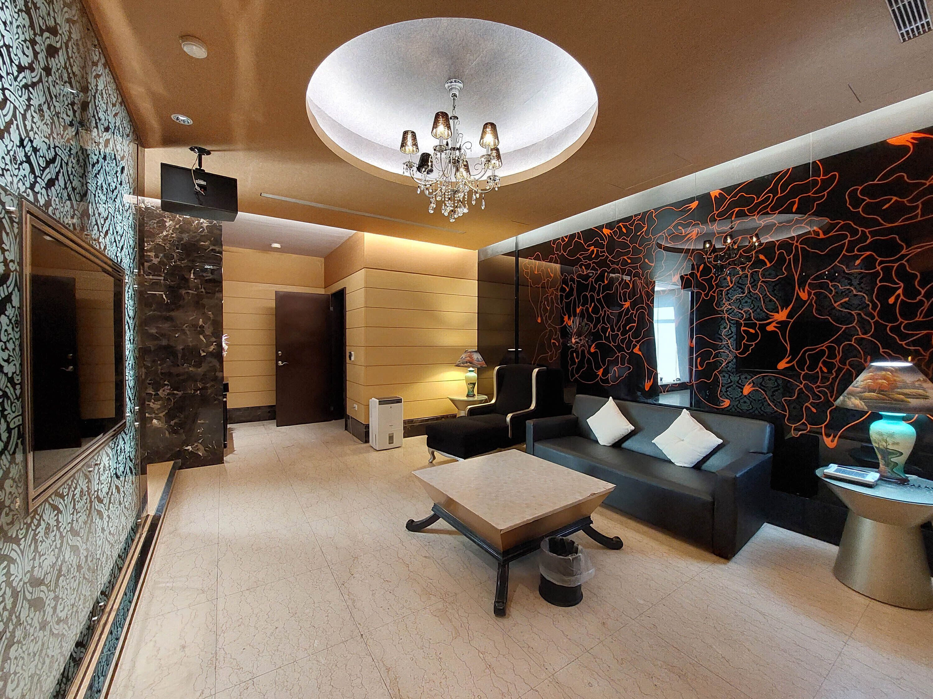 Uma sala de estar moderna com um lustre, um conjunto de sofás, uma mesa de centro e um painel decorativo.