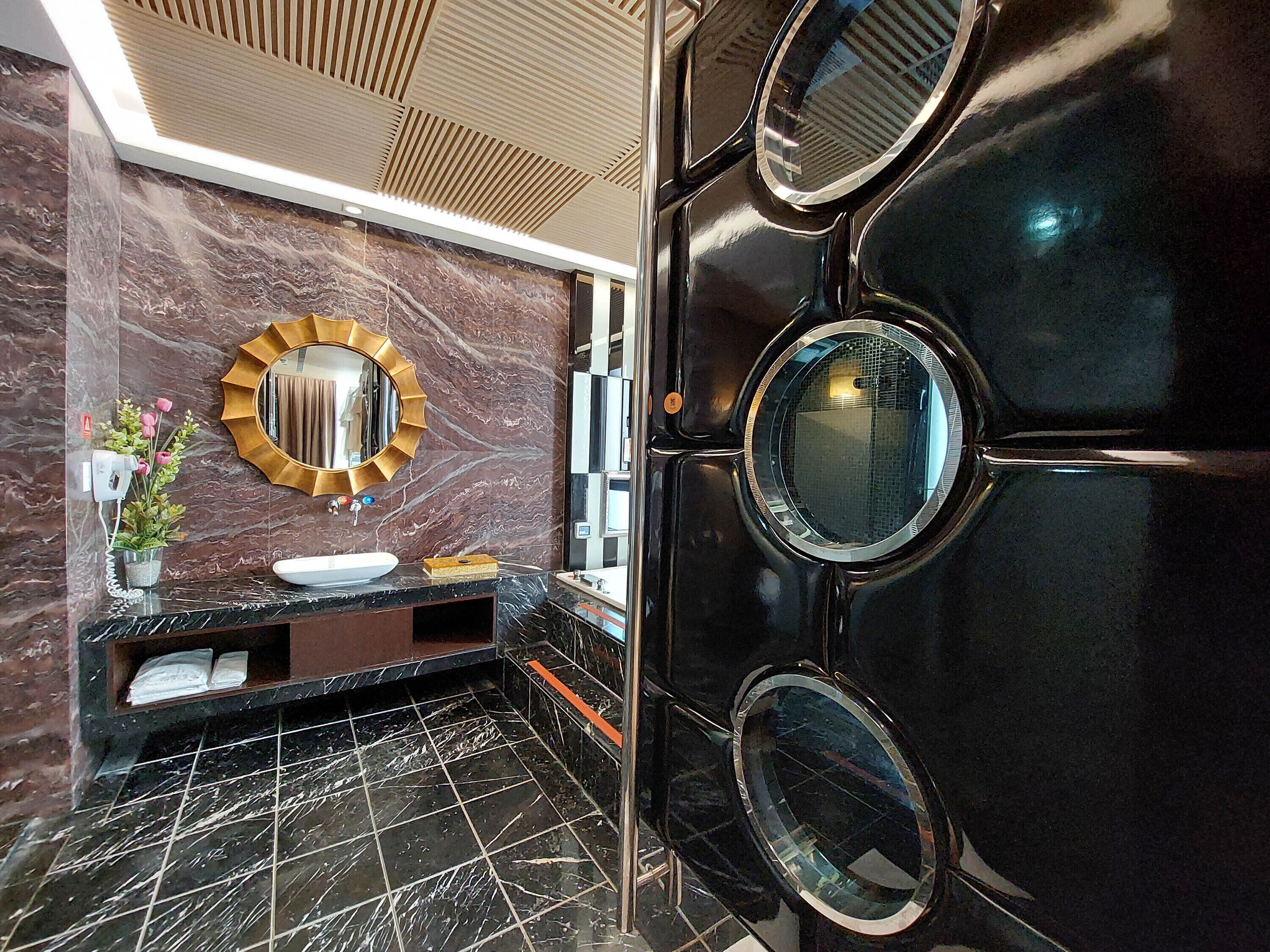A modern bathroom with a marble vanity, a round mirror, and a black door with circular mirrors.