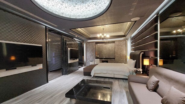 A modern bedroom with a large bed, a sofa, a TV, and a unique ceiling design. - ELYSEES MOTEL (Toufen)