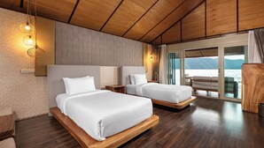 A hotel room with two beds, wooden flooring, a brick wall, and a large window with a view of the sea. - Ruknam Resort (Si Sawat)