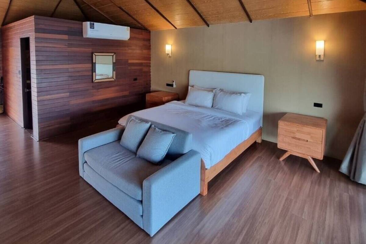 A bedroom with a sloped ceiling, a bed, a sofa, bedside tables, and wall-mounted lighting.