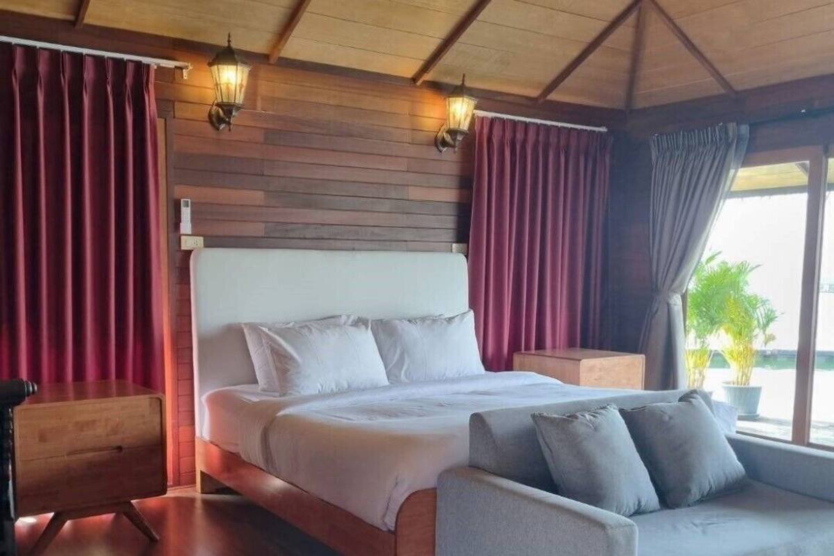 A bedroom with a bed, a sofa, wooden flooring, and a ceiling with wooden beams.