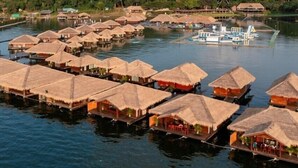 Overwater bungalows with thatched roofs on stilts, a boat docked nearby, and a mountain in the background. - Ruknam Resort (Si Sawat)