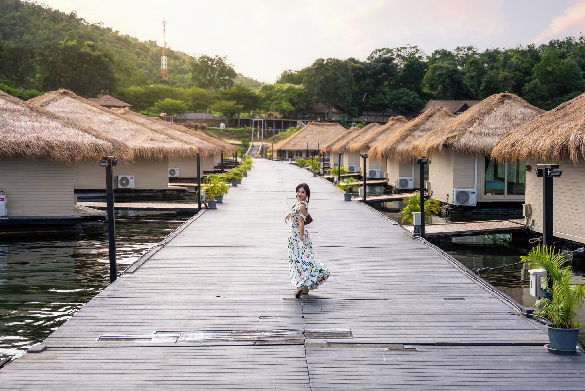 A wooden pier leading to overwater bungalows with thatched roofs and air conditioning units.