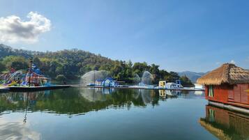 Enjoy a serene lakeside retreat with a water park, fountains, and a traditional hut amidst lush green surroundings.