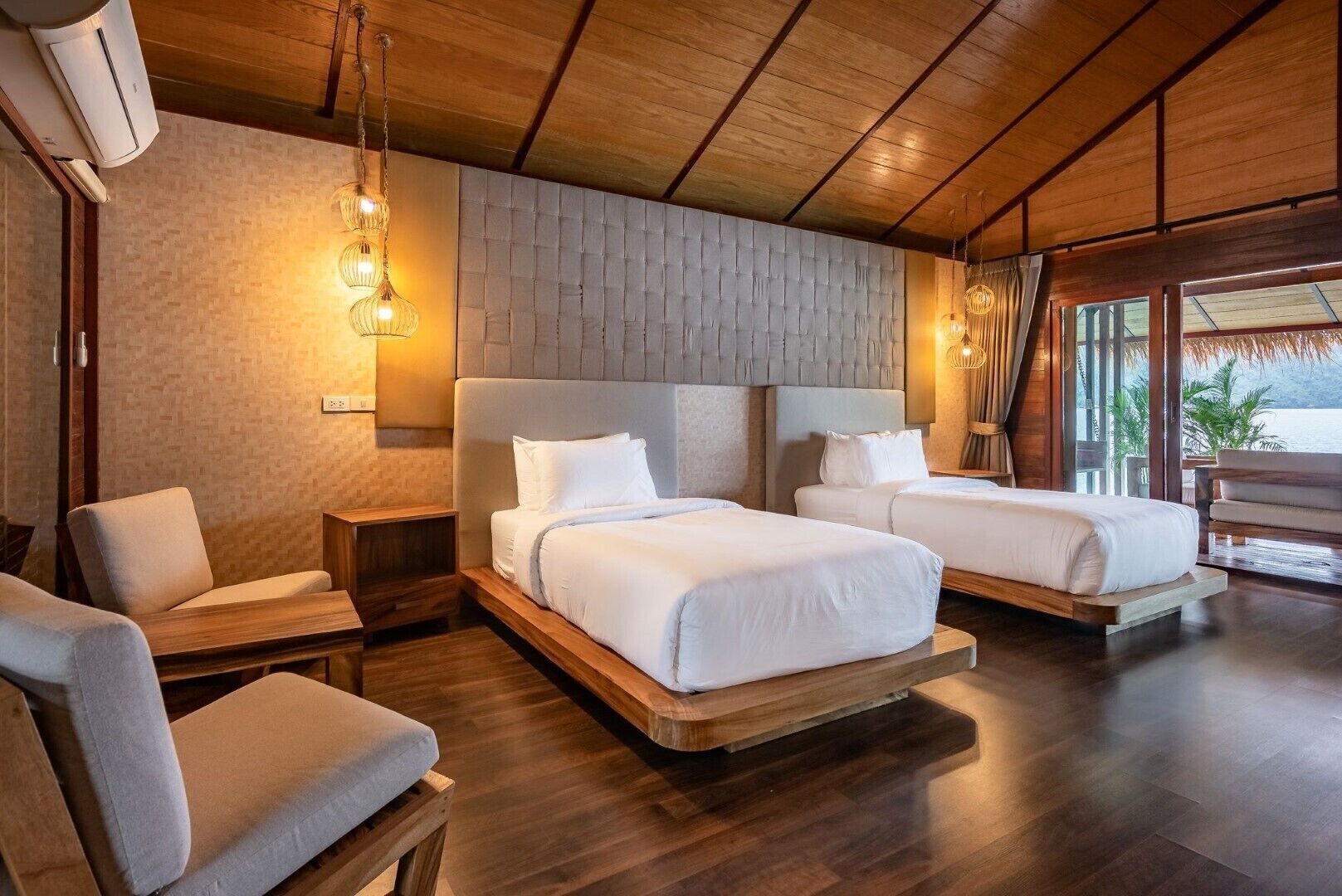 Habitación de hotel con dos camas, techo de madera, pared de ladrillo y vista al océano.