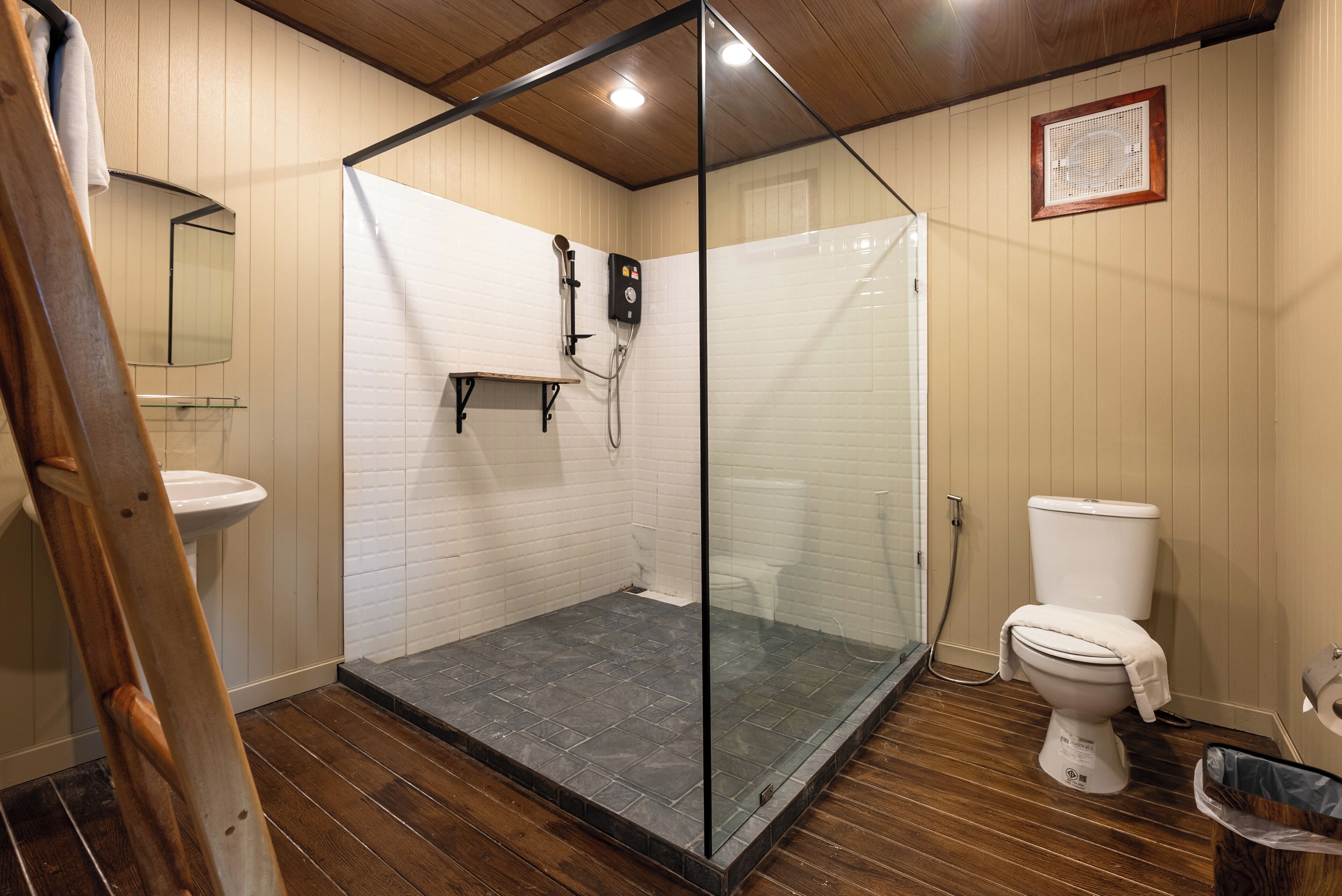 A bathroom with a glass-enclosed shower, a white toilet, and a wooden floor.