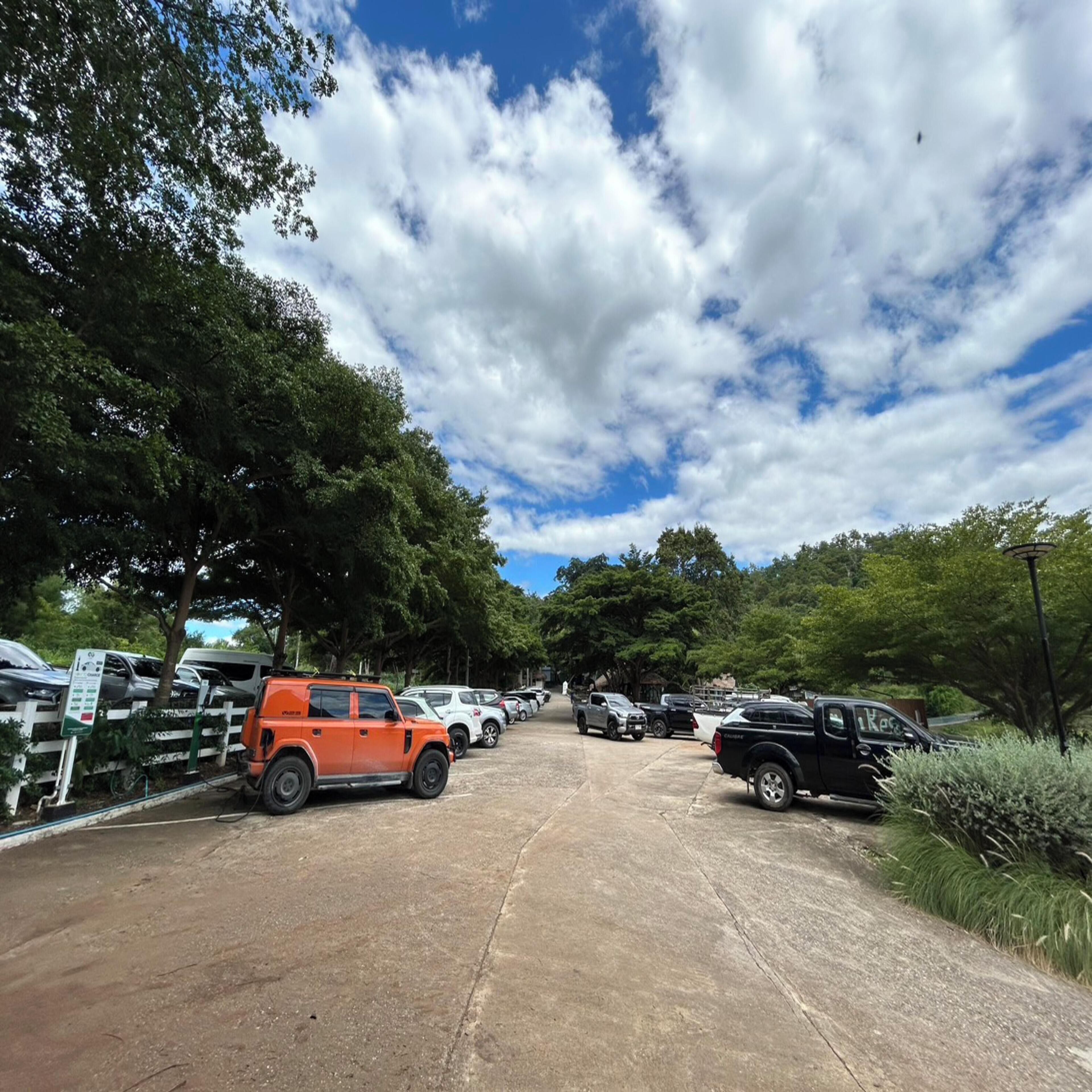 A parking lot with various vehicles, including a red SUV and a black pickup truck, under a partly cloudy sky.