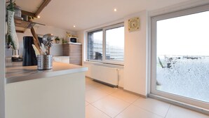 A modern kitchen with a large window, a radiator, and a view of a snowy landscape. - Lovely holiday home in Gros Chêne with bubble bath (Gros Chêne)