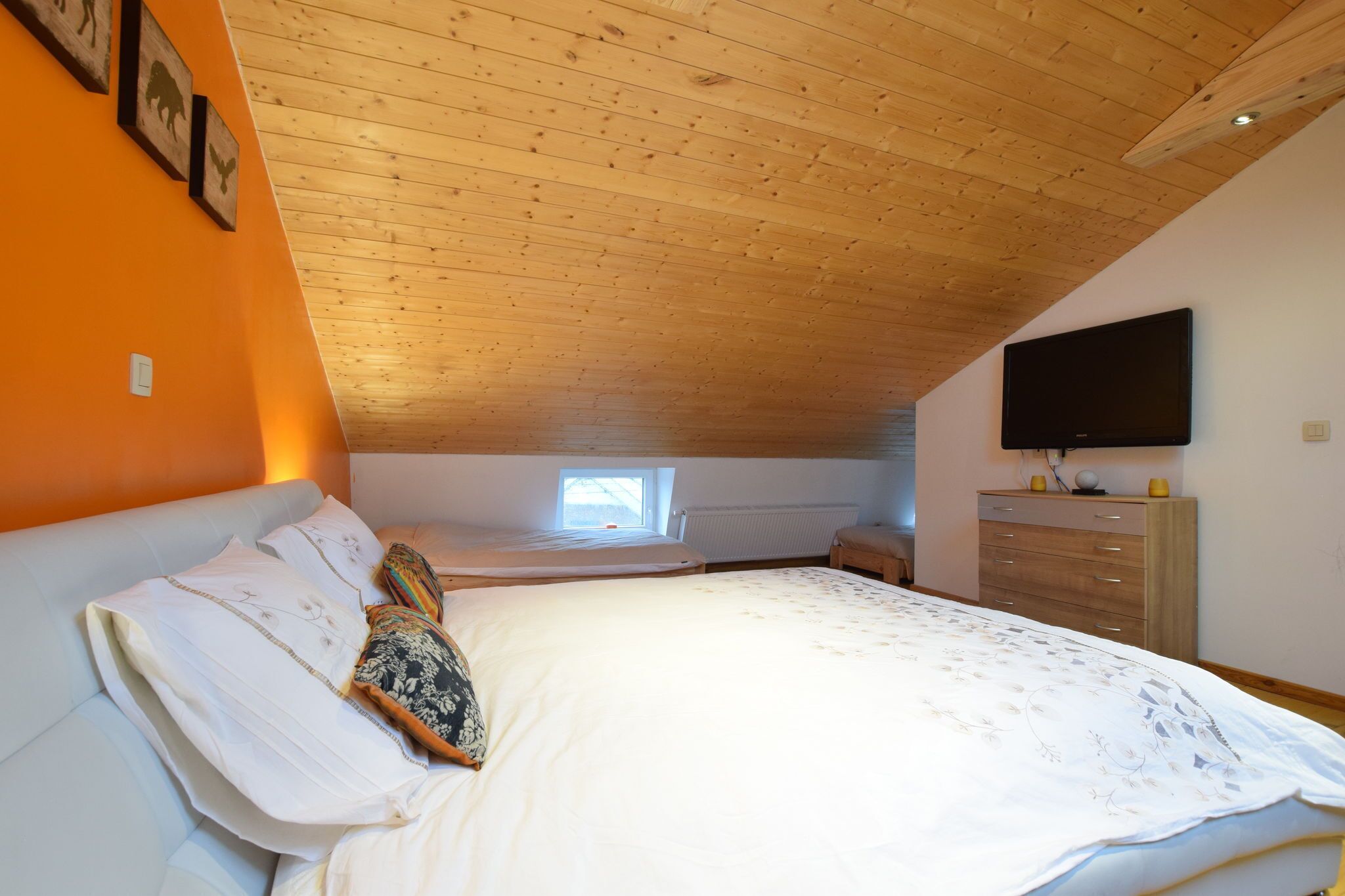 Un dormitorio con techo de madera, una cama con ropa de cama blanca, un aparador y un televisor en la pared.