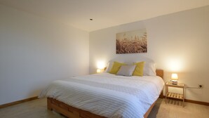 A bedroom with a wooden bed, white bedding, two bedside lamps, and a wall-mounted artwork. - Lovely holiday home in Gros Chêne with bubble bath (Gros Chêne)