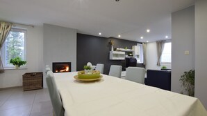A modern dining area with a long table, chairs, a fireplace, and a kitchen in the background. - Lovely holiday home in Gros Chêne with bubble bath (Gros Chêne)